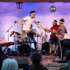 Sänger in 80s Kostüm macht auf der Bühne einen Luftspagat 